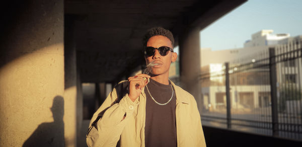 Portrait of young man wearing sunglasses while standing against wall