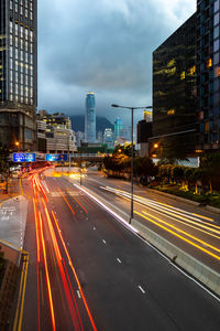 Light trails on city street against cloudy sky