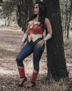 Full length portrait of young woman standing on tree trunk in forest