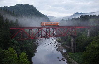 Train on bridge over river against sky during foggy weather