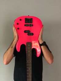 Young man holding guitar in front of face while standing against wall