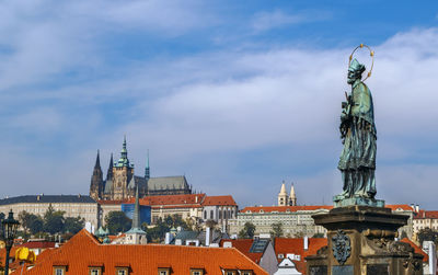 Statue of buildings in city against cloudy sky