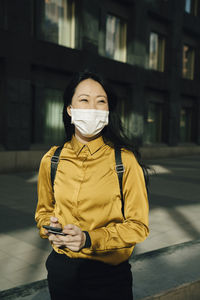 Happy woman with face mask holding smartphone