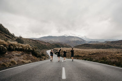 Friends running on road against sky