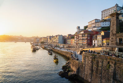 Buildings by sea against sky during sunset