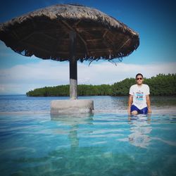 Young man sitting in poolside against blue sky