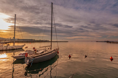 Sailboats moored in sea against sky during sunset