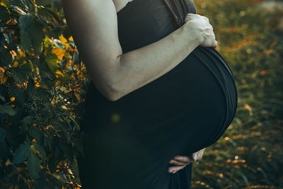 Pregnant woman hugging her tummy standing outdoors surrounded by nature. pregnancy, expectation