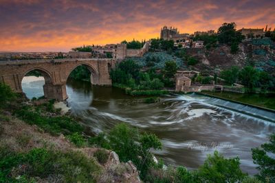 Arch bridge over river against sky during sunset