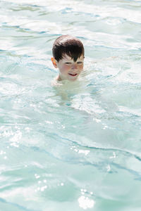 High angle of cute little boy with wet dark hair swimming in outdoor swimming pool during summer holidays