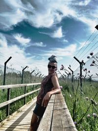 Full length of woman sitting on railing against sky