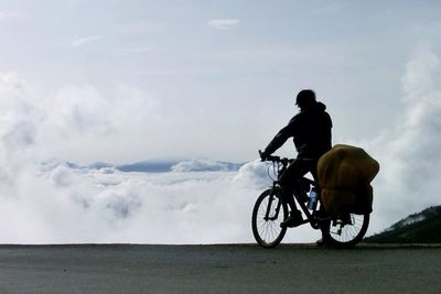 Silhouette bicycling against clouds