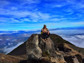 Male hiker relaxing on top of rocky mountain against blue sky