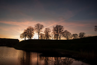 Silhouette trees by lake against sky during sunset