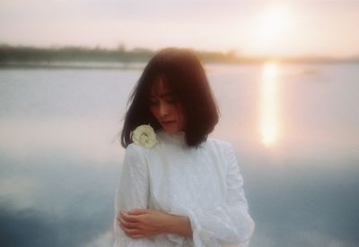 Woman standing by lake against sky during sunset