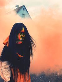 Portrait of young woman standing against orange sky