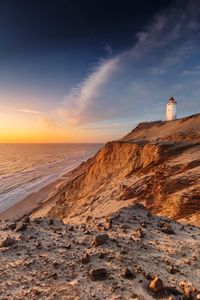 Lighthouse on beach by sea against sky during sunset