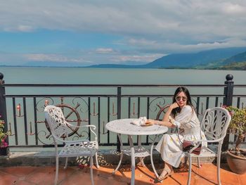 Portrait of woman sitting on chair at table against sky