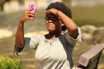 Young woman shielding eyes while taking selfie outdoors