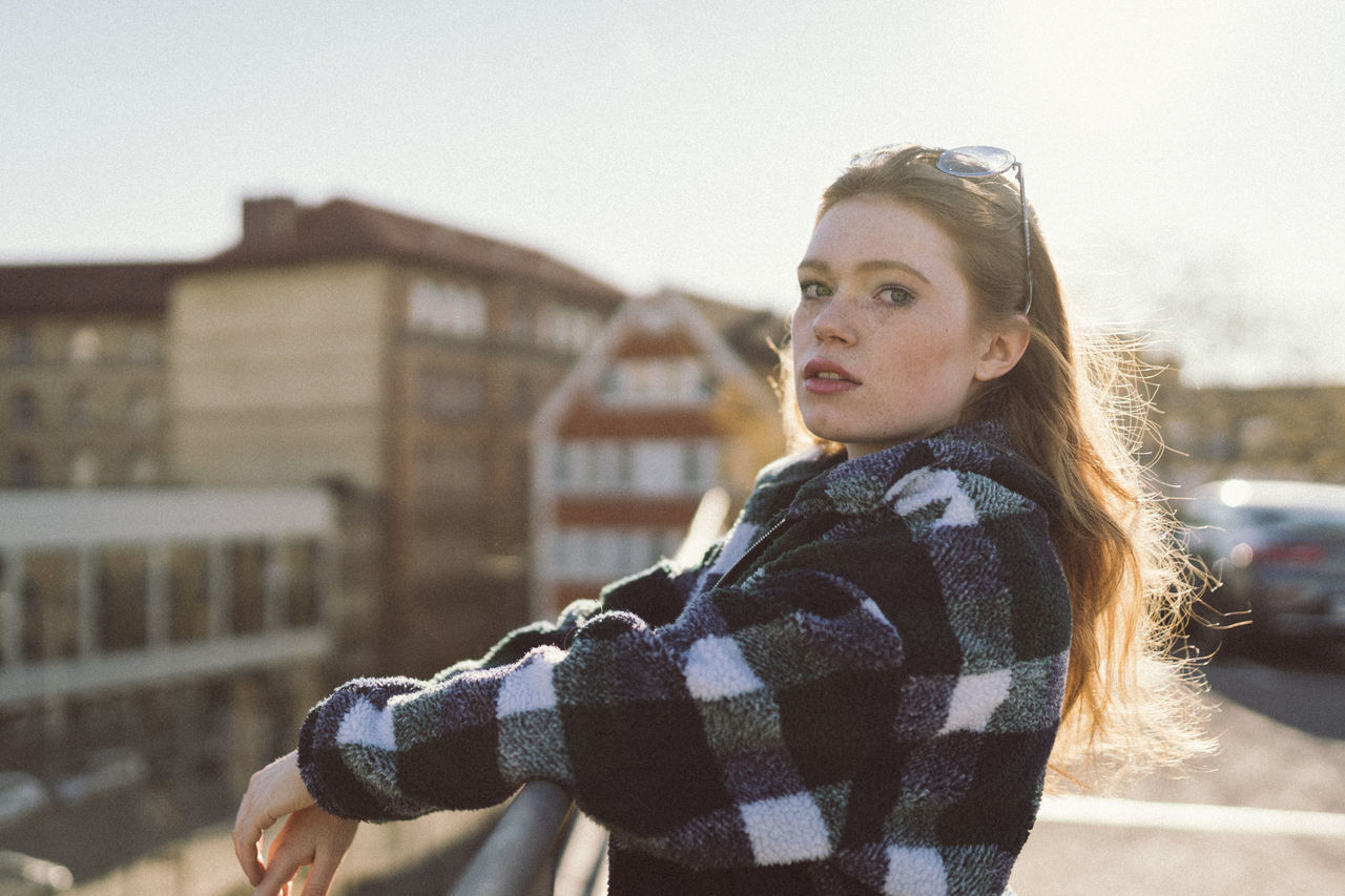 one person, focus on foreground, real people, architecture, young adult, lifestyles, standing, portrait, young women, leisure activity, built structure, building exterior, looking away, nature, city, looking, casual clothing, winter, outdoors, warm clothing, lens flare, teenager, beautiful woman, contemplation