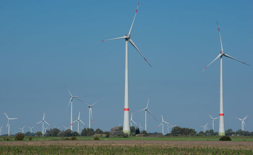 Windmills on field against clear blue sky