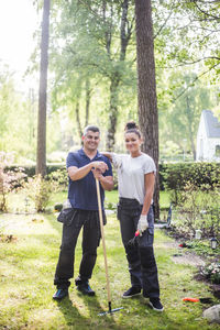 Full length portrait of smiling female trainee standing with hand on instructor's shoulder at garden