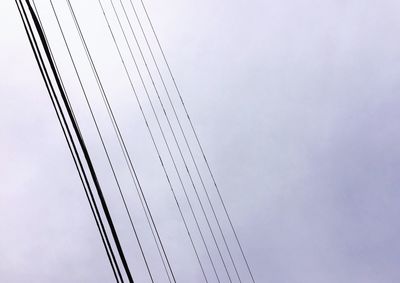 Low angle view of birds perching on cable against sky