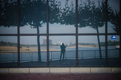 Men standing by railing against sky reflecting on building window