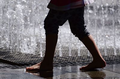 Low section of person walking by fountain on wet footpath