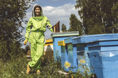 Happy beekeeper with bee smoker standing by wooden boxes on sunny day