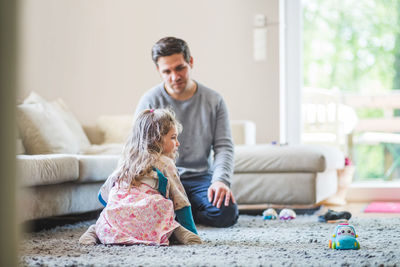 Father looking at daughter kneeling on carpet at home