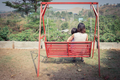 Rear view of mother and daughter sitting on large swing