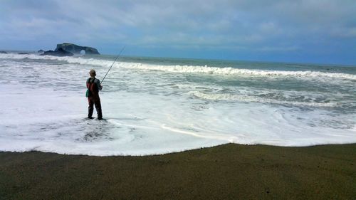 Rear view of man fishing on shore at beach