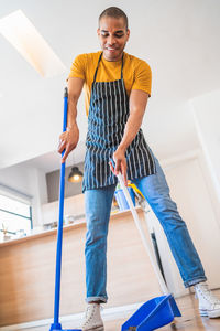 Mid adult man wearing apron while cleaning with equipment at home