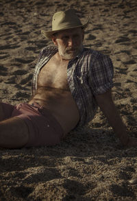 Adult man in hat with open shirt sitting on beach