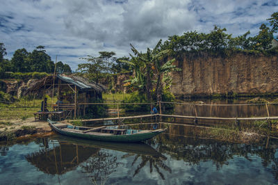 Boat moored on river by trees against sky