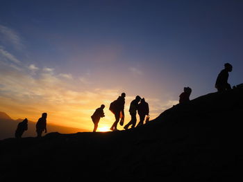Silhouette people on shore against sky during sunset