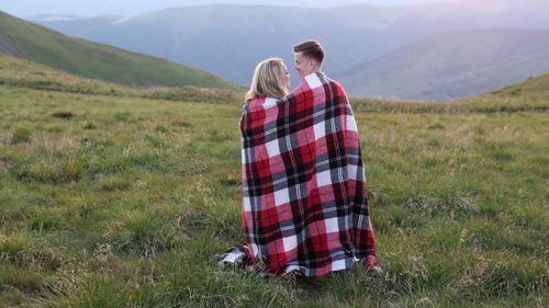 Couple wrapped in blanket standing on field