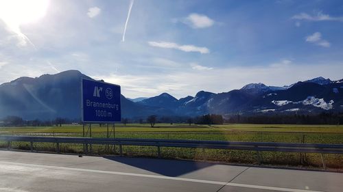 Road sign on field by mountains against sky