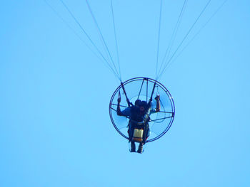 Low angle view of man paramotoring against clear blue sky