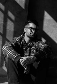 Young man looking away while standing against wall