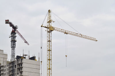 Low angle view of cranes at construction site against sky