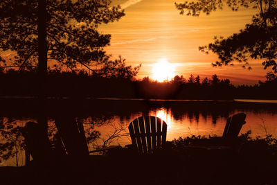 Silhouette trees by lake against orange sky