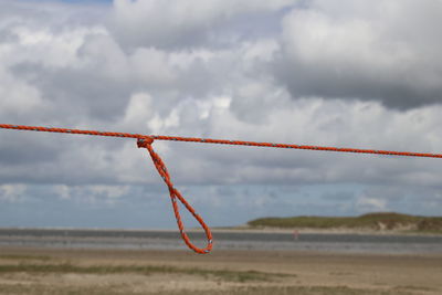 Red wire hanging on rope against sky