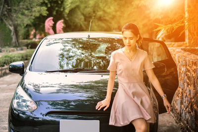 Young woman leaning on car during sunset