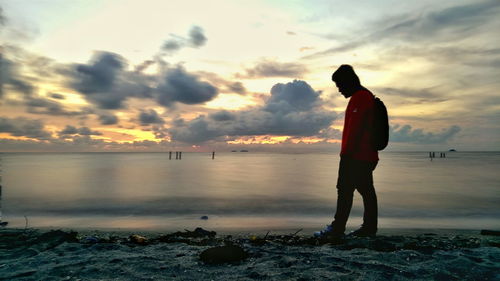 Side view of man standing at beach against sky during sunset