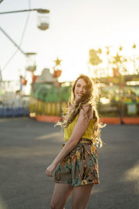 Delighted female dancing looking at camera with raised arms at fairground and enjoying summer weekend