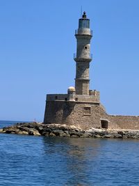 Lighthouse by sea against clear sky