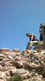 Low angle view of people on rocks against clear blue sky