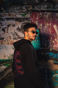 Side view of young man standing against graffiti wall